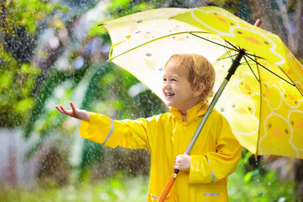 Photo of Child playing in the rain. Kid with umbrella.