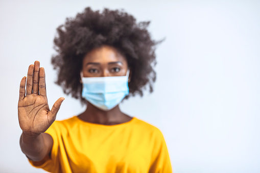Photo of African american young woman showing stop sign, wearing protection face mask against corona virus