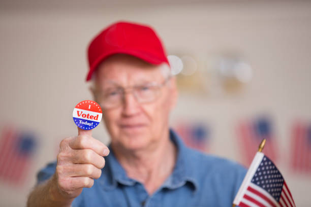 Voters at Polling Place Senior man votes on election Day.  He shows off his I VOTED sticker. voter id stock pictures, royalty-free photos & images