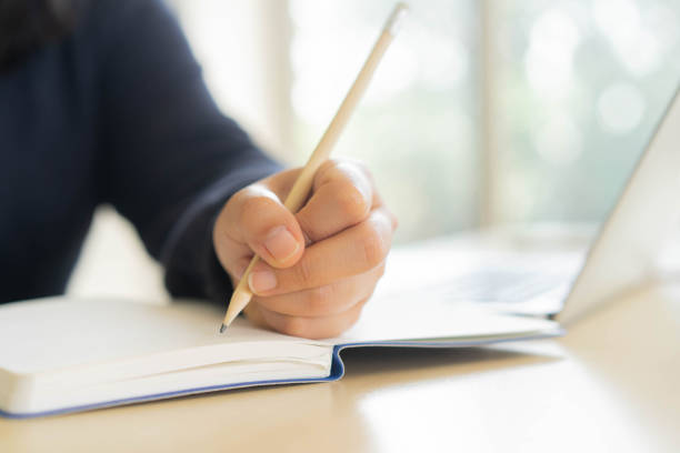 istock close up woman hand using pencil to writing homework or practice exam before test while opening laptop to learning from webinar for e-learning new normal lifestyle concept 1270978056