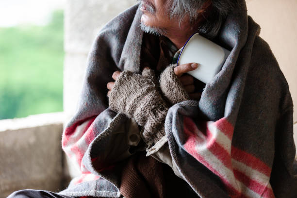 бедный старый бездомный азиат сидит с грязным одеялом, перчатки сидит холодно в углу заброшенного здания. - tramp стоковые фото и изображения
