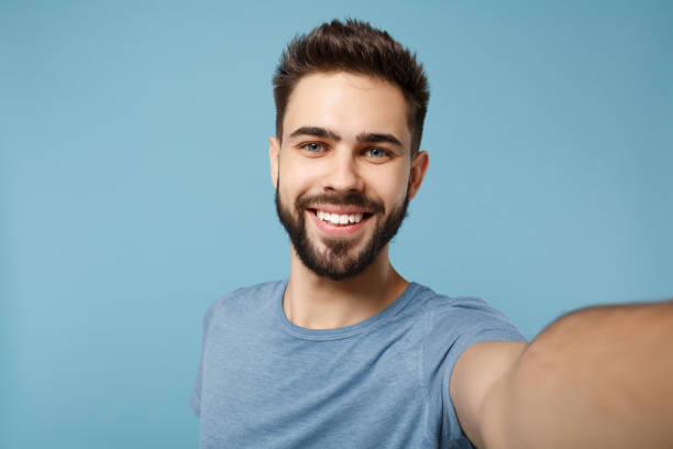 nahaufnahme junger lächelnder mann in lässiger kleidung posiert isoliert auf blauem wandhintergrund, studioporträt. menschen aufrichtige emotionen lifestyle-konzept. verspotten sie den kopierraum. selfie-aufnahmen auf dem handy. - selfie stock-fotos und bilder