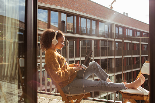 Young woman is using a laptop, working from the balcony of her apartment