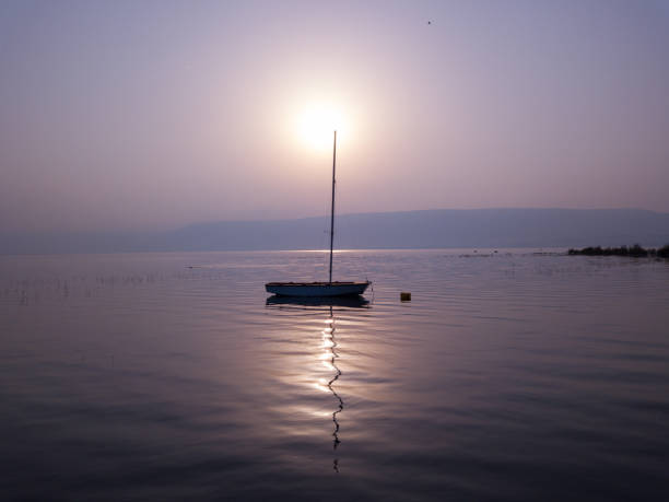 湖の上の日の出。驚くべき夕日の下で穏やかな水の上に浮かぶボート。 - lake tiberius ストックフォトと画像