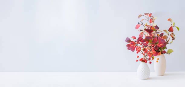 istock Home interior with decor elements. Colorful autumn leaves in a vase on a light background 1270996479
