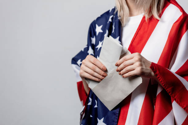 istock girl with USA flag holds envelope with a vote on white background 1271001476