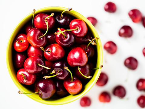 Overhead shot of a bowl of cherries and several cherries on a white background.