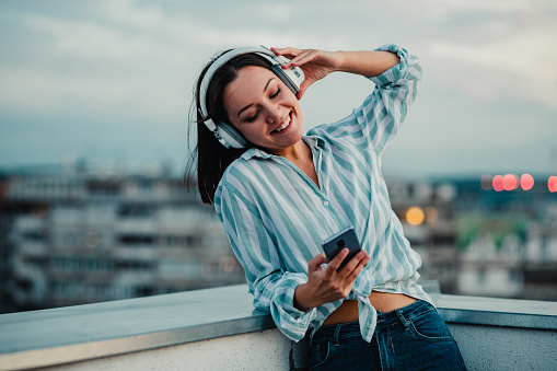 Woman on the rooftop listening music with headphones and holding smart phone