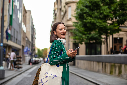 Young business woman after work on the street, holding smart phone and smiling