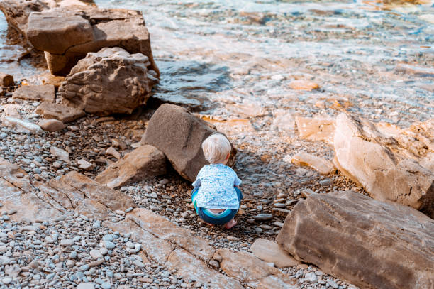 Cute little boy playing outdoors by the sea Cute little caucasian boy playing outdoors by the sea. baby squatting stock pictures, royalty-free photos & images
