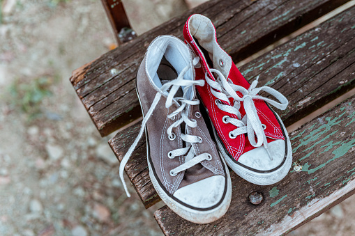 Close up of a pair of worn canvas shoes on the old wooden bench, one is red and other is grey.