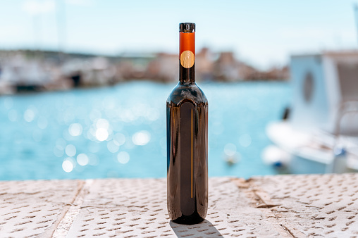 Close up image of a dark wine bottle outdoors by the sea.