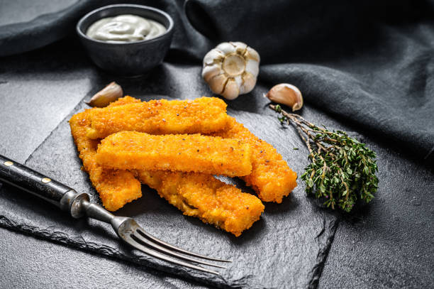 Crispy fried fish fingers with breadcrumbs served with sauce tartar. Black background. Top view Crispy fried fish fingers with breadcrumbs served with sauce tartar. Black background. Top view. fish stick stock pictures, royalty-free photos & images
