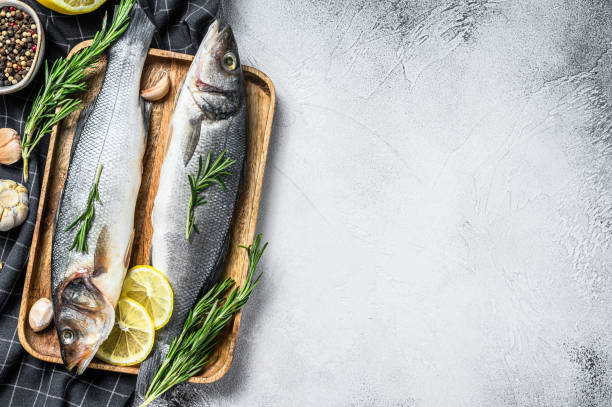 istock Raw sea bass fish with herbs and lemon. White background. Top view. Copy space 1271012490