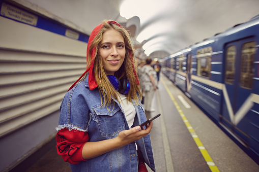 Smiling woman is standing in underground station near an arriving train. Young girl  in red hoodie stands in subway.