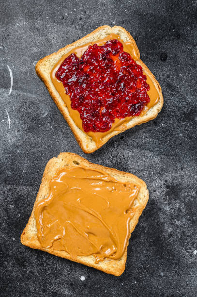 istock Peanut butter and jelly on white bread toasts.  Black background. Top view 1271015964