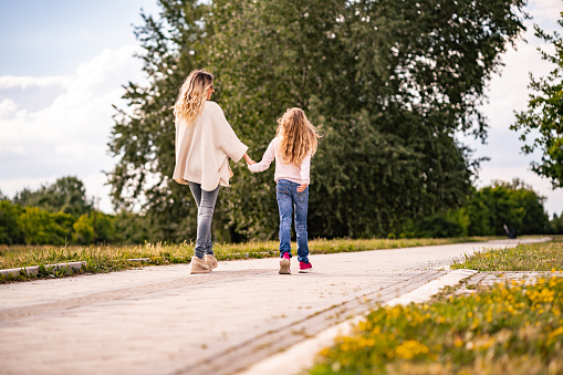 Child holds her mother's hand and they walk on a sunny day