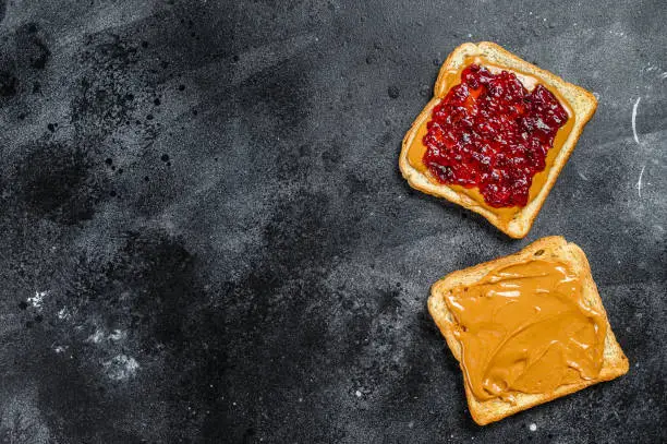 Peanut butter sandwich  toast with berry jam.  Black background. Top view. Copy space.