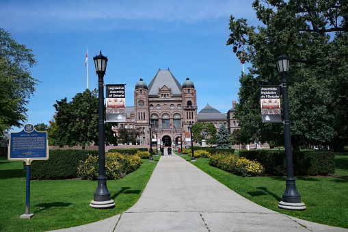 Toronto, Canada - September 6, 2020: View of the Ontario provincial Parliament Building in Queen's Park, with a  plaque describing its history.