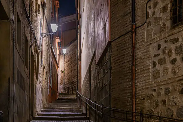 Photo of lighthouses illuminating an alley and staircase in the historic center of the city of toledo at night. Spain