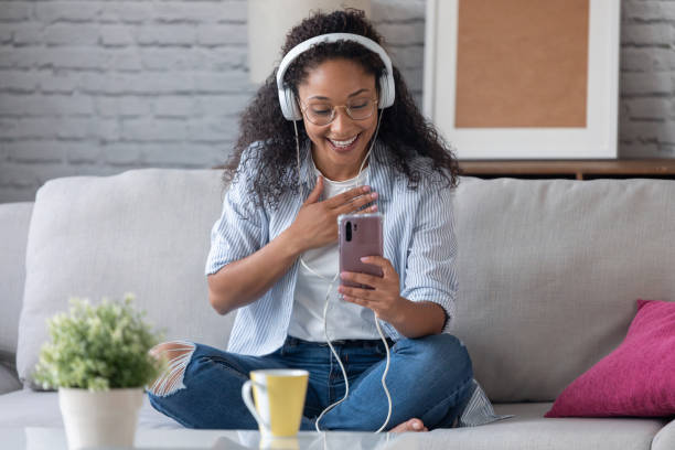 istock Beautiful young woman having video conversation with friends with headphones while using her smartphone sitting on sofa at home. 1271019873
