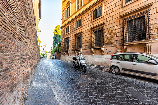 Rome, Italy - September 5, 2018: Italian cobblestone street outside in historic city in morning and woman motorcycle in morning