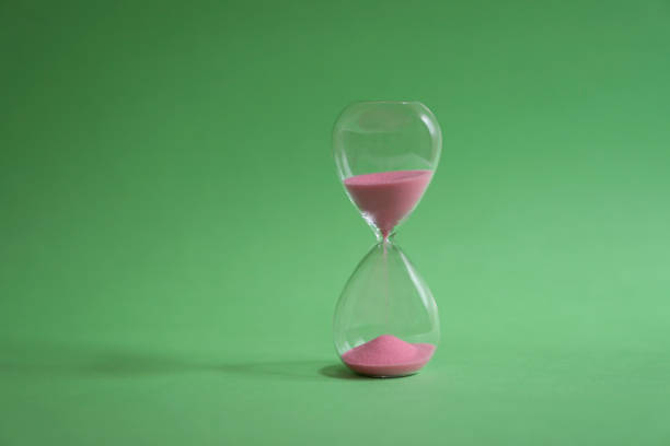 Hourglass with sand flowing on green background. Time passing or classic timer concept.