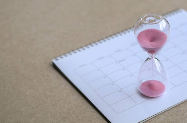 istock Hourglass with sand flowing, on top of calendar. Copy space. 1271027308