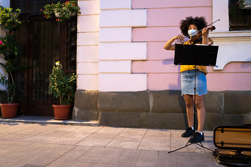 Young afro street musician with protective face masks playing violin on the street in time of pandemic