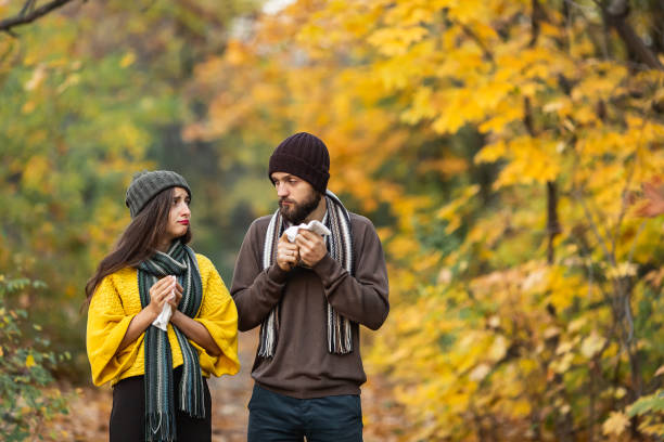 uomo malato e ragazza starnutire e soffiare il naso in autunno nel parco - autumn women leaf scarf foto e immagini stock