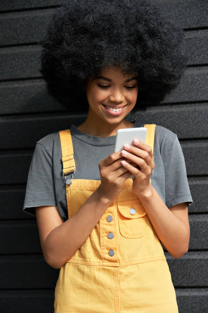 istock Smiling African young hipster  lady with Afro hair using smartphone. 1271031459