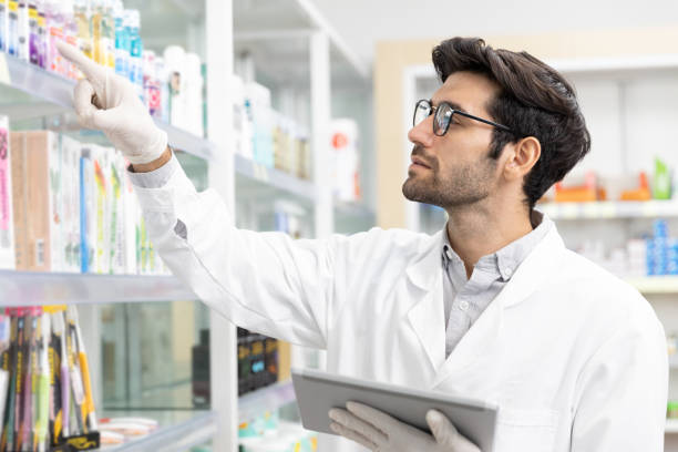 farmacéutico masculino que revisa la farmacia de stock utilizando la tecnología de tabletas digitales en farmacia moderna. - pharmacy medicine pharmacist storage room fotografías e imágenes de stock