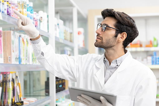 Business owner Middle eastern male pharmacist checking stock drugstore using digital tablet technology in modern pharmacy.