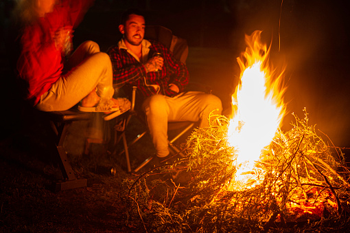 Young caucasian couple relaxing in front of camping outdoor fire.