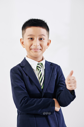 Portrait of cheerful diligent Vietnamese schoolboy showing thumbs-up and smiling at camera