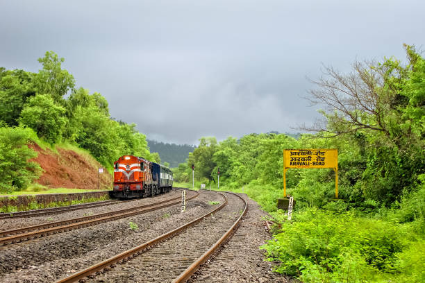 indian railway's passenger carrying train entering a beautiful, scenic , small aravali road station, surrounded by lush green environment. - non urban scene railroad track station day imagens e fotografias de stock