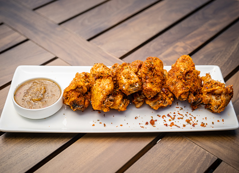 A mouthwatering plate of delicious chicken wings covered in a rich and textured dry rub. The white plate sits on a wood table.