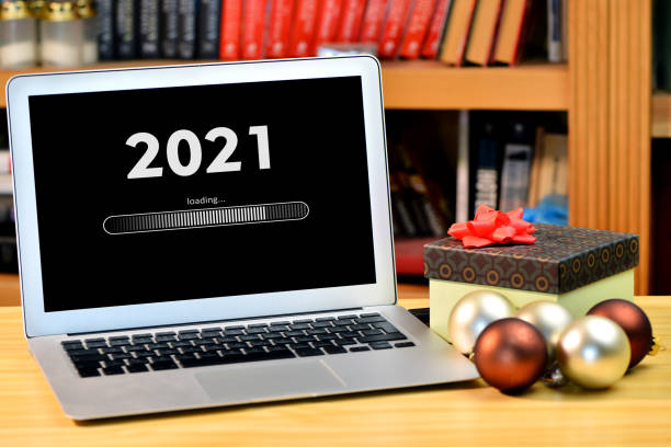 istock on the table christmas decorations, gift box and laptop with text - 2021 loading - on screen, blurred shelf with books in the background 1271056019