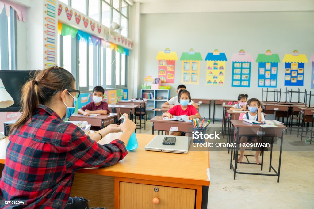 Group of school kids with teacher sitting in classroom online and raising hands,Elementary school. Teacher wearing protective mask to Protect Against Covid-19,Group of school kids with teacher sitting in classroom online and raising hands,Elementary school,Learning and people concept. Classroom Stock Photo