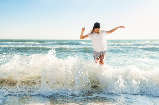 Funny young woman playful on sunset beach. Beautiful happy female on the shore of the blue sea having fun playing splashing water, positive mood, summer vacation, sunny concept