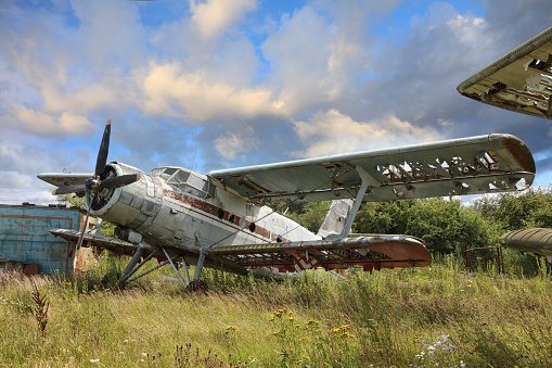 Abandoned small propeller aircraft plane standing in the field against cloudy blue sky