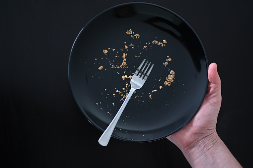 Point of view of a person holding an empty black plate with breadcrumbs.