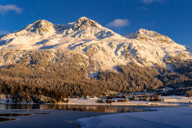 blick auf wunderschöne schneeberge hinter dem silvaplana-see und seinem dorf in der schweiz bei einem wintersonnenuntergang - engadine built structure house mountain stock-fotos und bilder