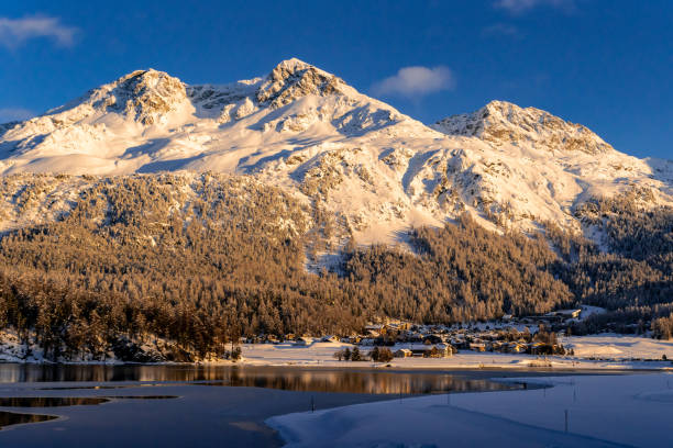 vista de hermosas montañas de nieve detrás del lago silvaplana y su pueblo en suiza durante una puesta de sol de invierno - st moritz engadine mountain winter fotografías e imágenes de stock