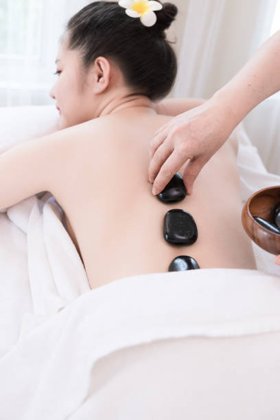 jeune femme asiatique obtenant le massage de spa avec le massage chaud de pierre - massaging spa treatment stone massage therapist photos et images de collection