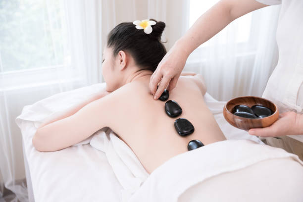 jeune femme asiatique obtenant le massage de spa avec le massage chaud de pierre - massaging spa treatment stone massage therapist photos et images de collection