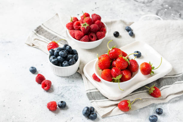 istock Ripe berries. Different berries in white ceramic bowls on a light table. Strawberries, raspberries and blueberries in plates against a white brick wall 1271081853