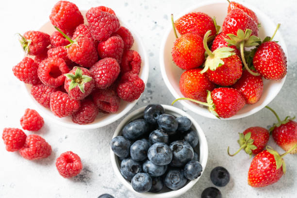 istock Ripe berries. Different berries in white ceramic bowls on a light table. Strawberries, raspberries and blueberries in plates 1271081857