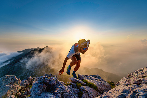 Sky runner man uphill on rocks at sunset