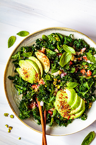 Healthy salad with kale, quinoa, nuts and avocado in a white bowl. Healthy vegan food concept.